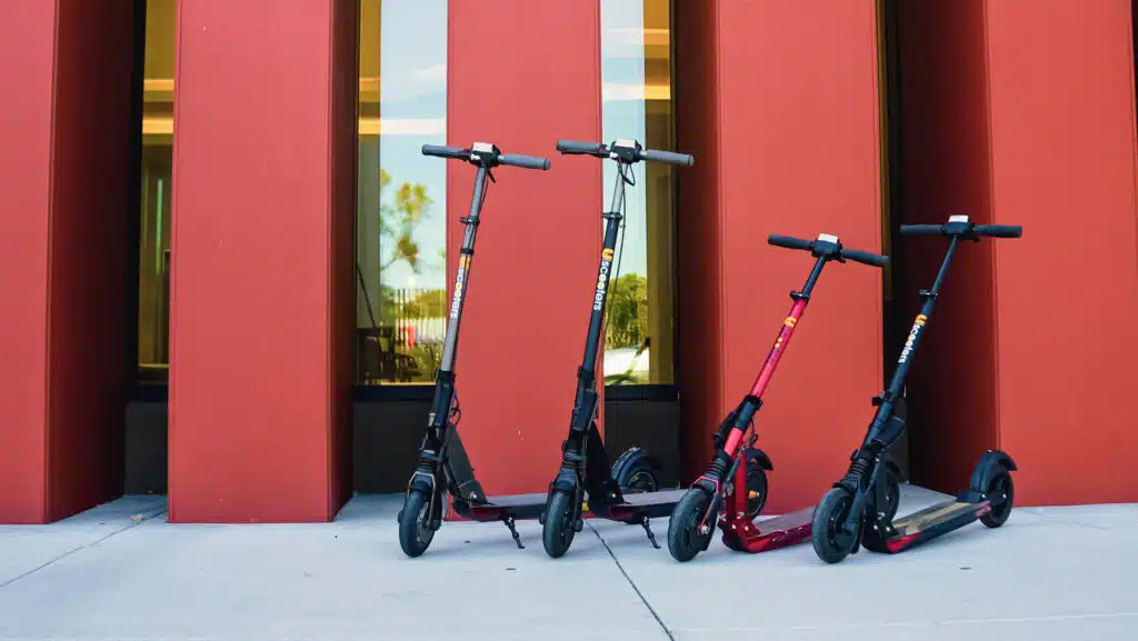 4 Uscooters GT Sport in front of red pillared building with glass windows