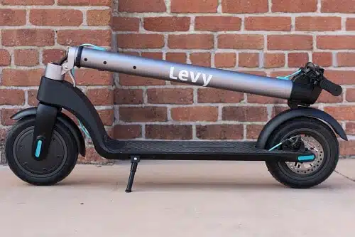 levy electric scooter folded in front of a brick wall