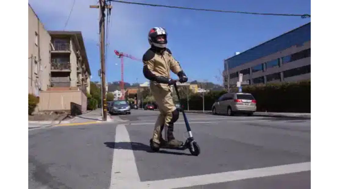A man in a motorcycle helmet turning on an electric scooter