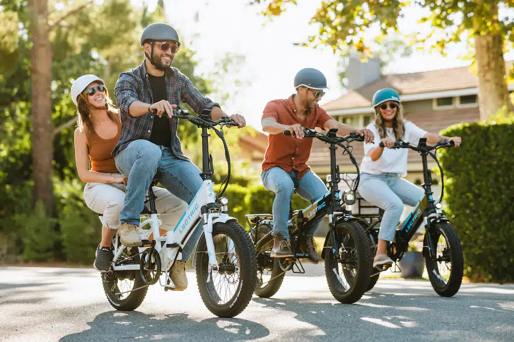 Smiling adults wearing helmets and riding Lectric e bikes
