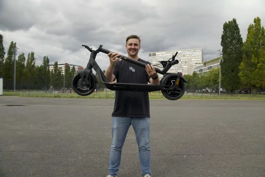 man smiling and holding up lightweight folded electric scooter