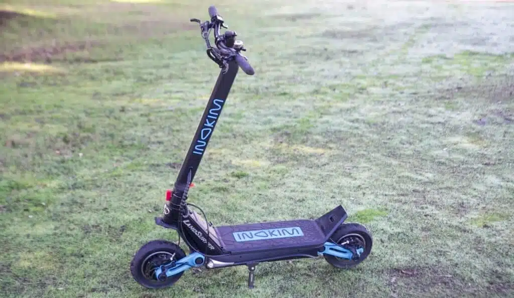 The Inokim OXO 2023, black with blue accents and lettering, in a sunlit field