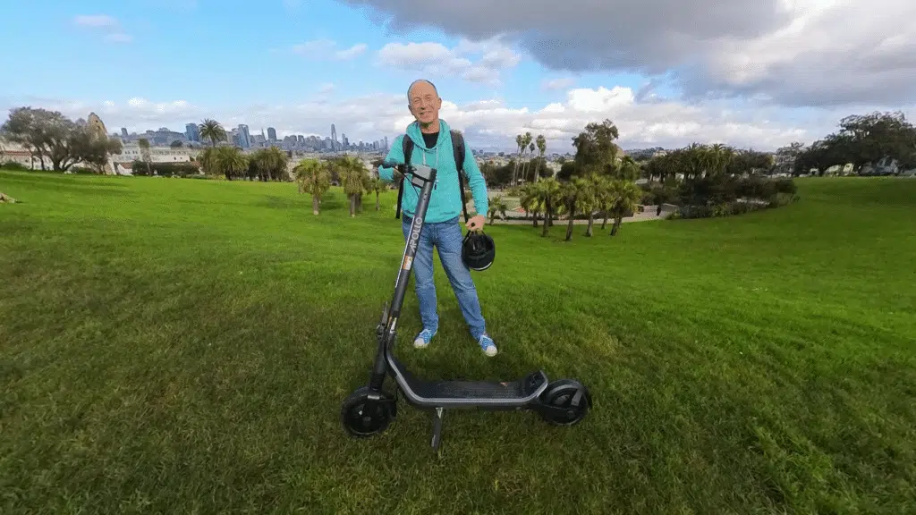 a man standing in a field behind the Apollo Go electric scooter