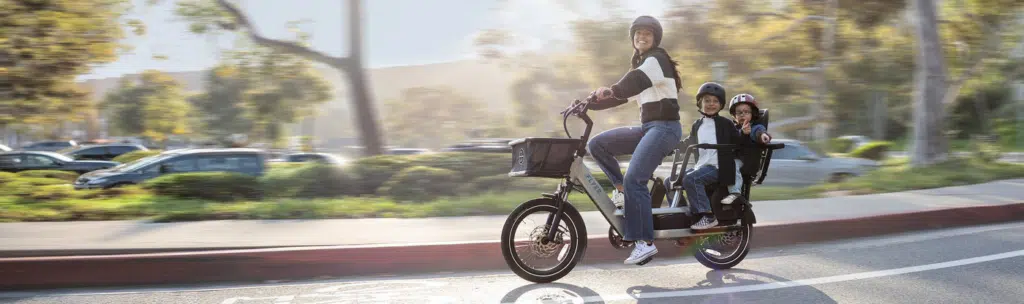 Parent riding an electric cargo bike with two kids - best family e-bikes